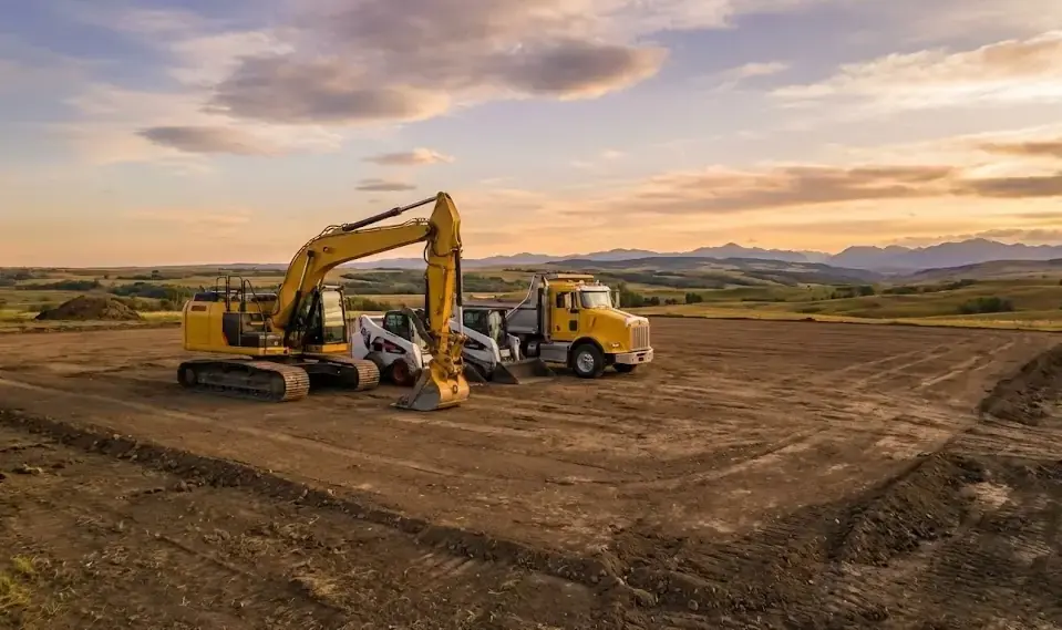 Bear Excavating fleet including excavator, skid steer, and dump truck on a graded site with Rocky Mountain foothills in the background